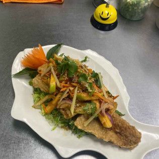 Garnished fried fish on a white plate with sliced onions and herbs on a gray table.
