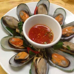 Plate of mussels arranged around a bowl of red dipping sauce with greens underneath
