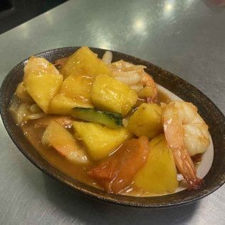 A bowl of yellow fruit pieces and shrimp in a glossy sauce on a table