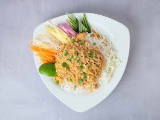 Colorful Vietnamese noodle salad with herbs, lime, and crushed peanuts on a white triangular plate