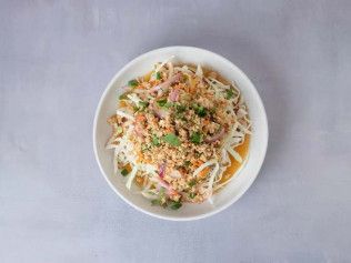 Bowl of noodle soup topped with shredded vegetables and herbs on a light surface