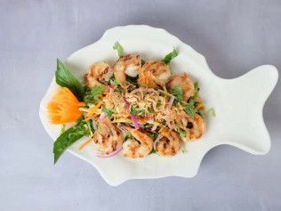 Shrimp salad with herbs and sliced orange garnish on a white fish-shaped plate