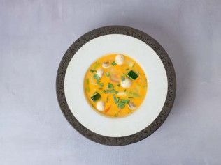 Top-down view of a bowl of yellow soup with vegetables on a white plate