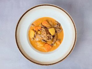 Top-down view of a bowl of orange soup with dumplings and sliced carrots