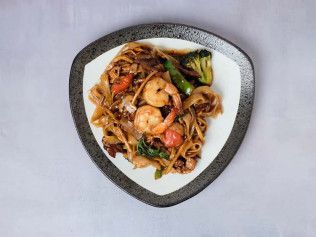 Plate of stir-fried noodles with shrimp and vegetables on a triangular white dish