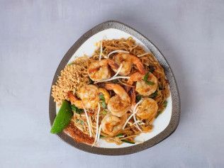 Shrimp noodle dish on a triangular plate, topped with bean sprouts and served with lime and peanuts