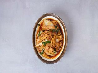 Oval bowl of noodle soup with vegetables and tofu on a white background
