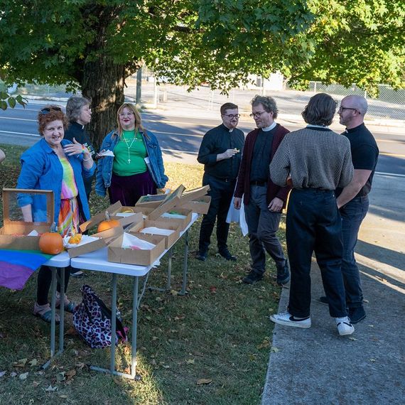 Group of people at a table with donuts; outdoors on a sunny day. Some are wearing religious collars.