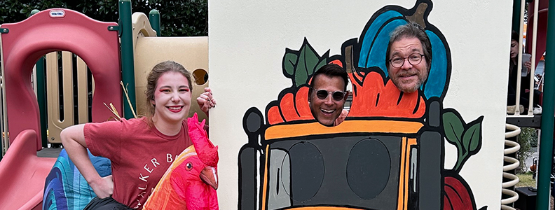 A young woman and two men posing for a photo with a fall-themed cutout on a playground.