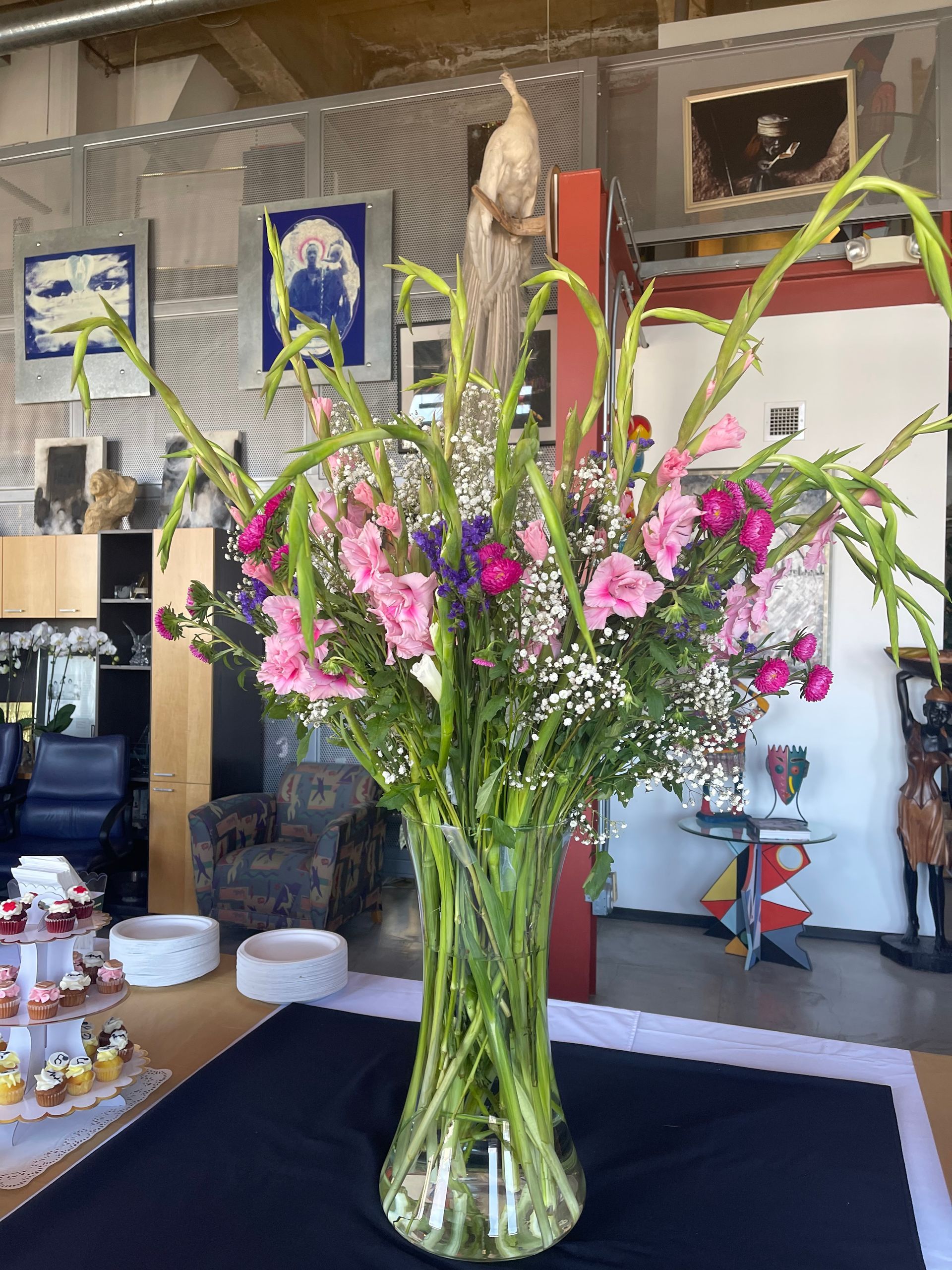 Glass vase of pink and green flowers on a table in a room with framed wall art