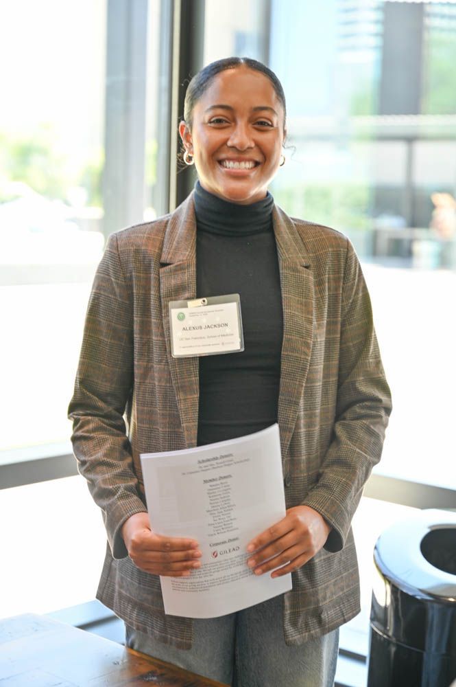 Smiling person holding papers and wearing a name badge in a bright indoor hallway