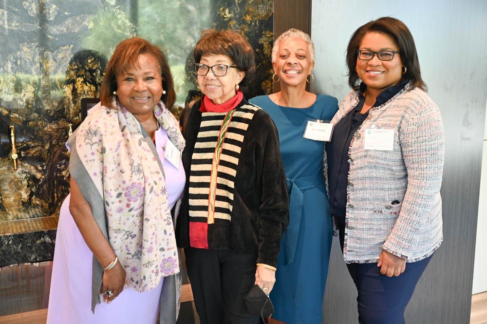 Four women standing together indoors, smiling at a formal event.