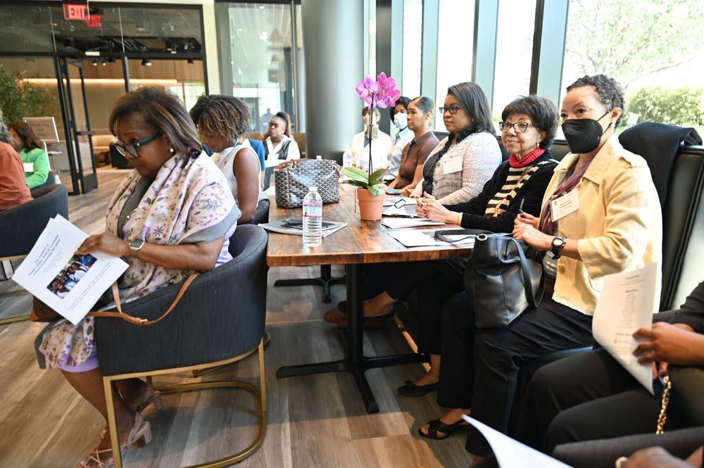 People seated at tables in a bright lobby, listening attentively during a meeting.