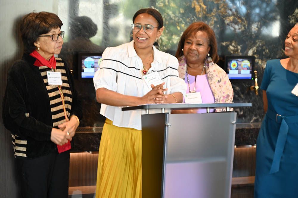 Four women stand at a podium, smiling during a public event.