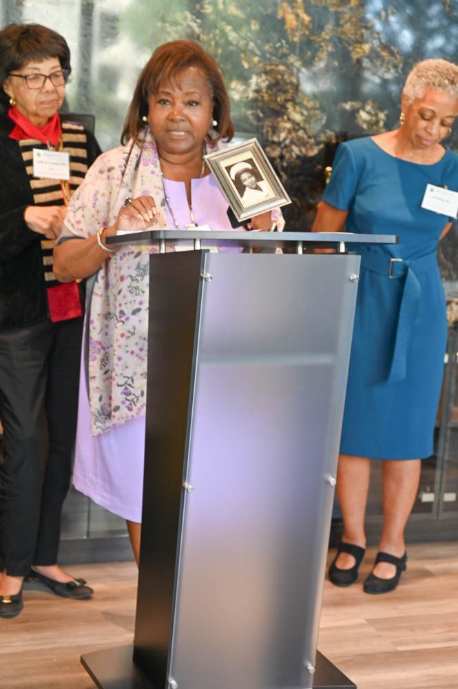 Woman speaking at a podium with two people standing behind her in a room.