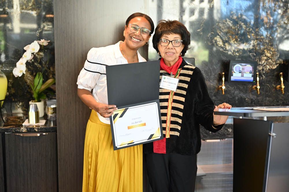 Two people smiling and posing with an award plaque at an indoor event
