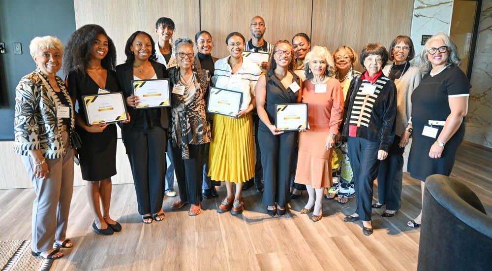 Group of people posing indoors, holding certificates in front of a wood-paneled wall.