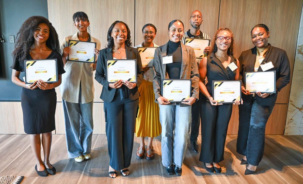 Seven people holding certificates stand in a line at a formal indoor event.