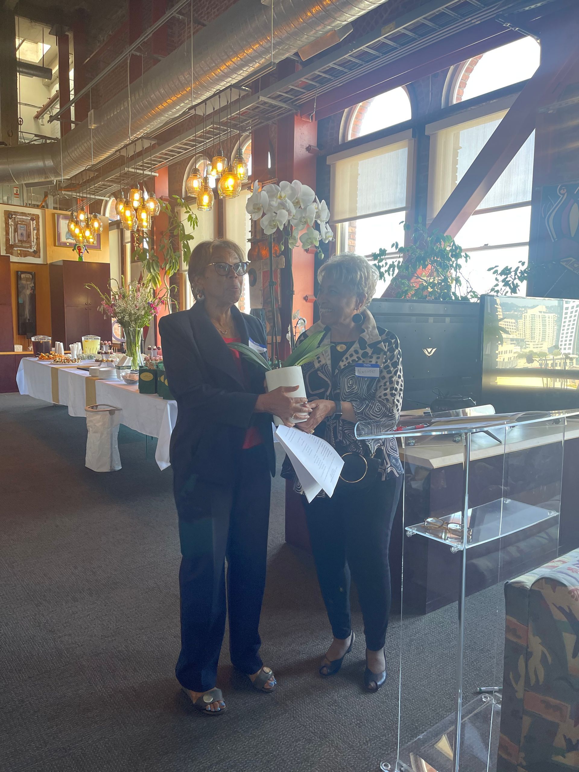 Two people standing in a decorated indoor venue near a buffet table and large windows