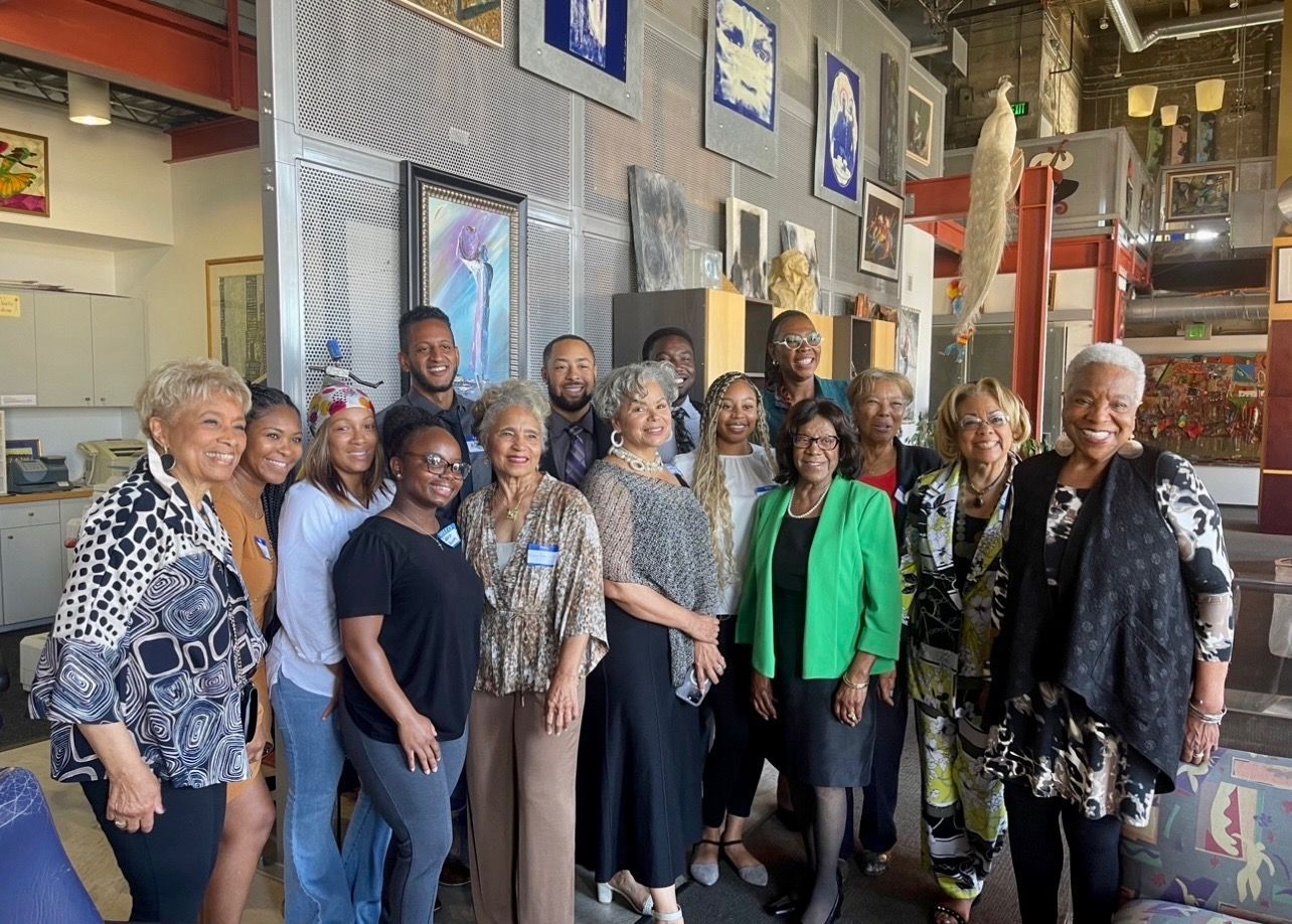 Group of people standing together in an indoor workshop or gallery, smiling at the camera.at Auxiliary to the Sinkler Miller Medical Association