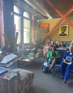People seated in a cozy room with large arched windows, artwork, and a projection screen at Auxiliary to the Sinkler Miller Medical Association