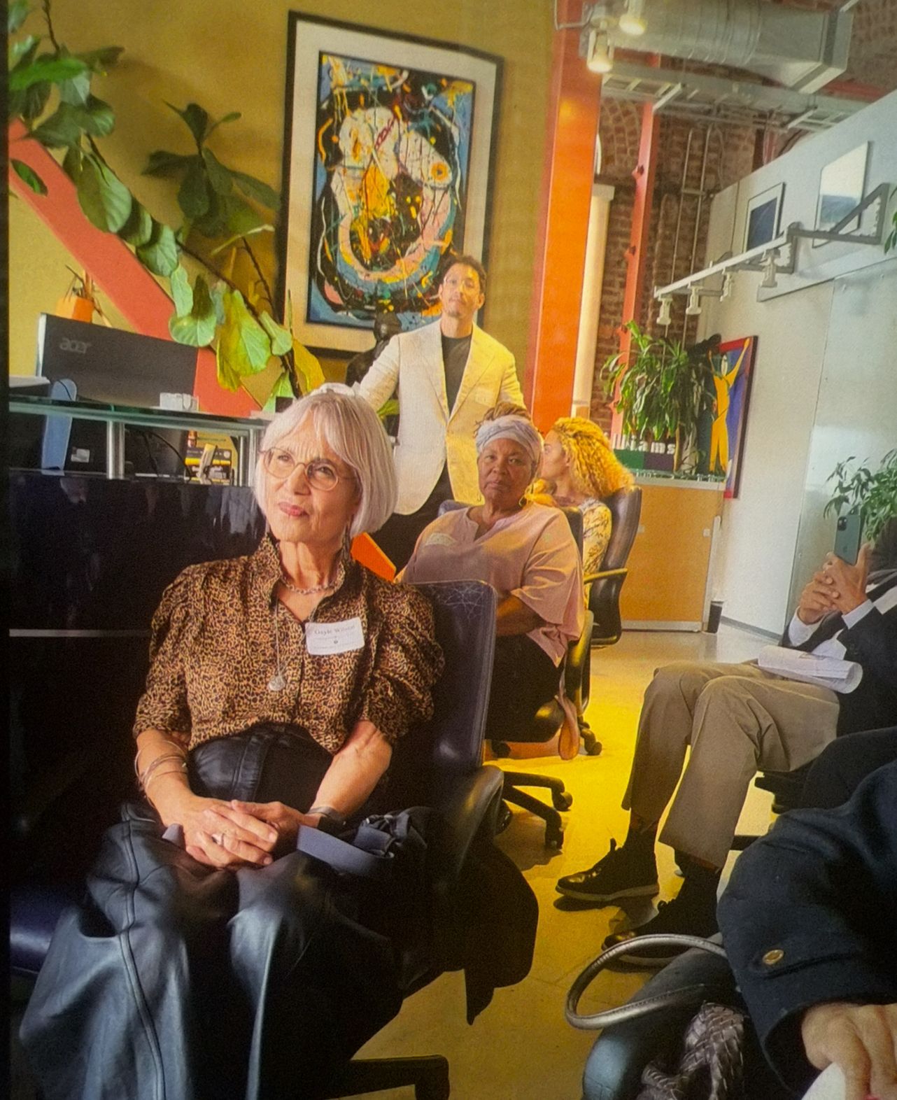 People seated in a warm, colorful indoor venue with a standing presenter in the background.