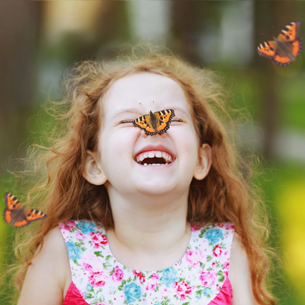 Laughing child with a butterfly on her nose in a flowered dress outdoors