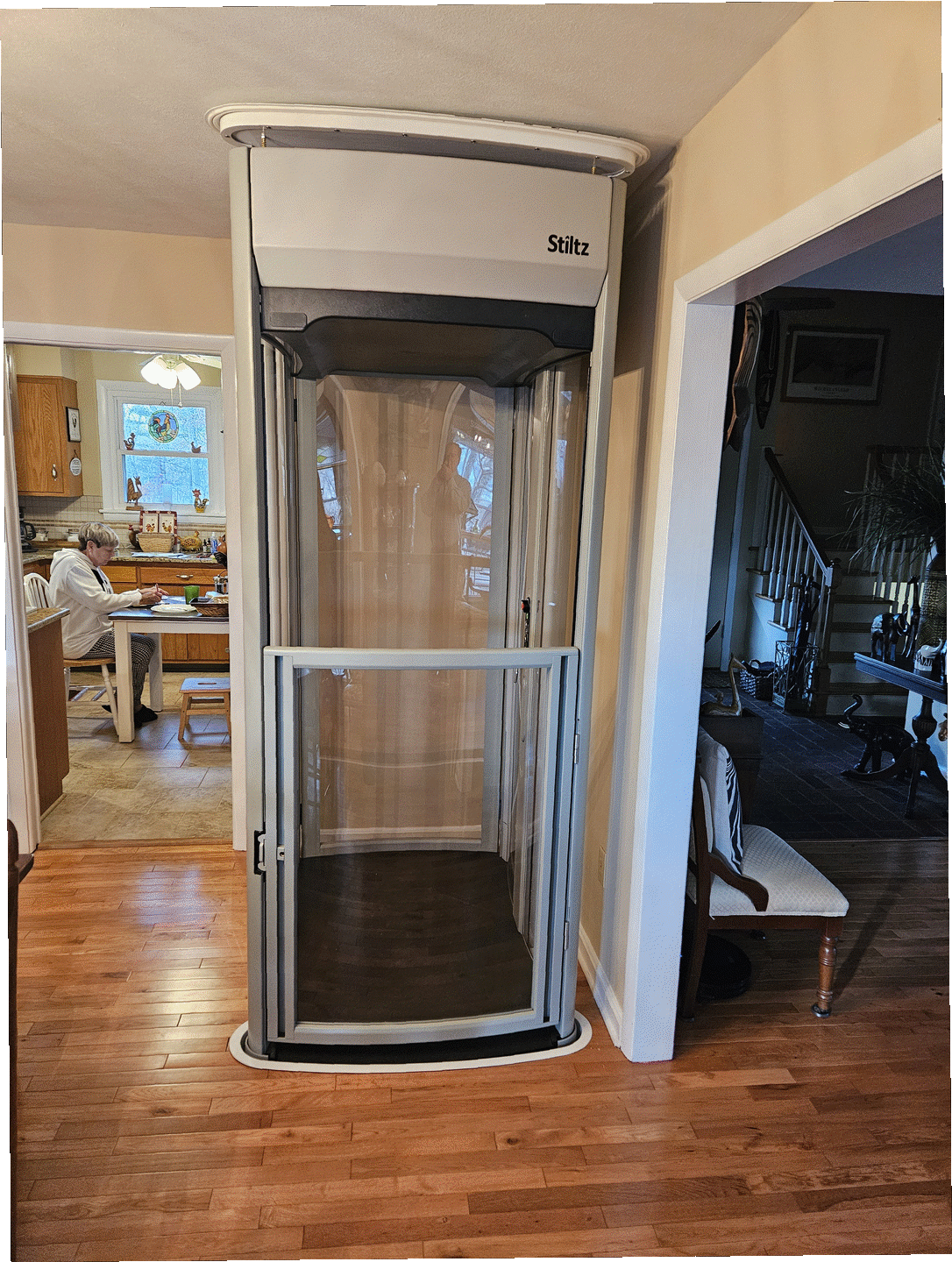 Home elevator with clear doors installed in a hallway beside a staircase.