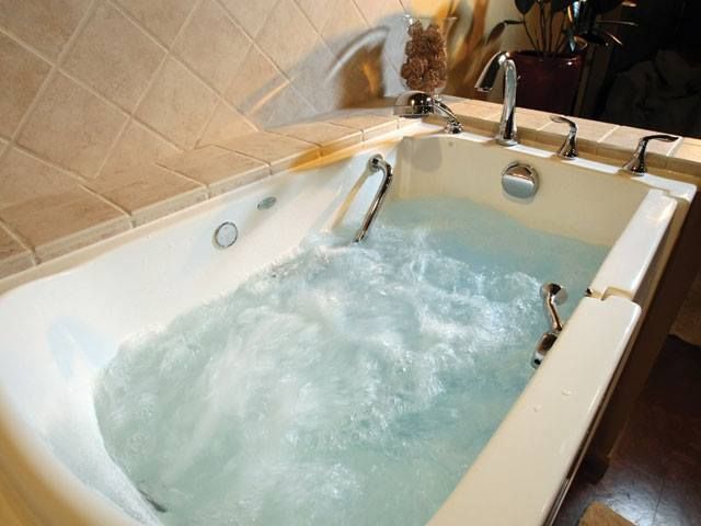 Running water filling a white bathtub with blue-tinted bubbles in a tiled bathroom