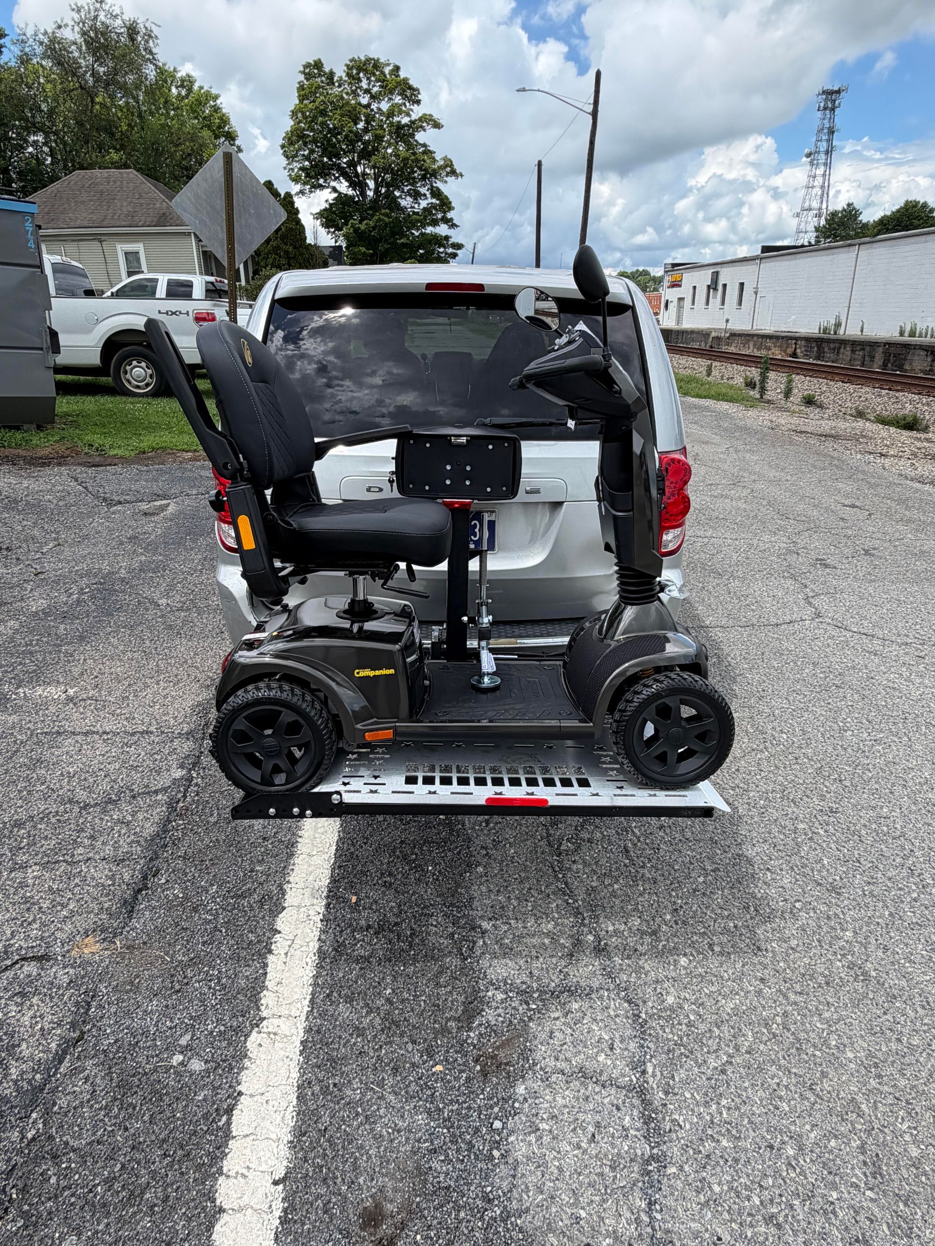 Wheelchair attached to the back of a black car in a parking lot on a cloudy day