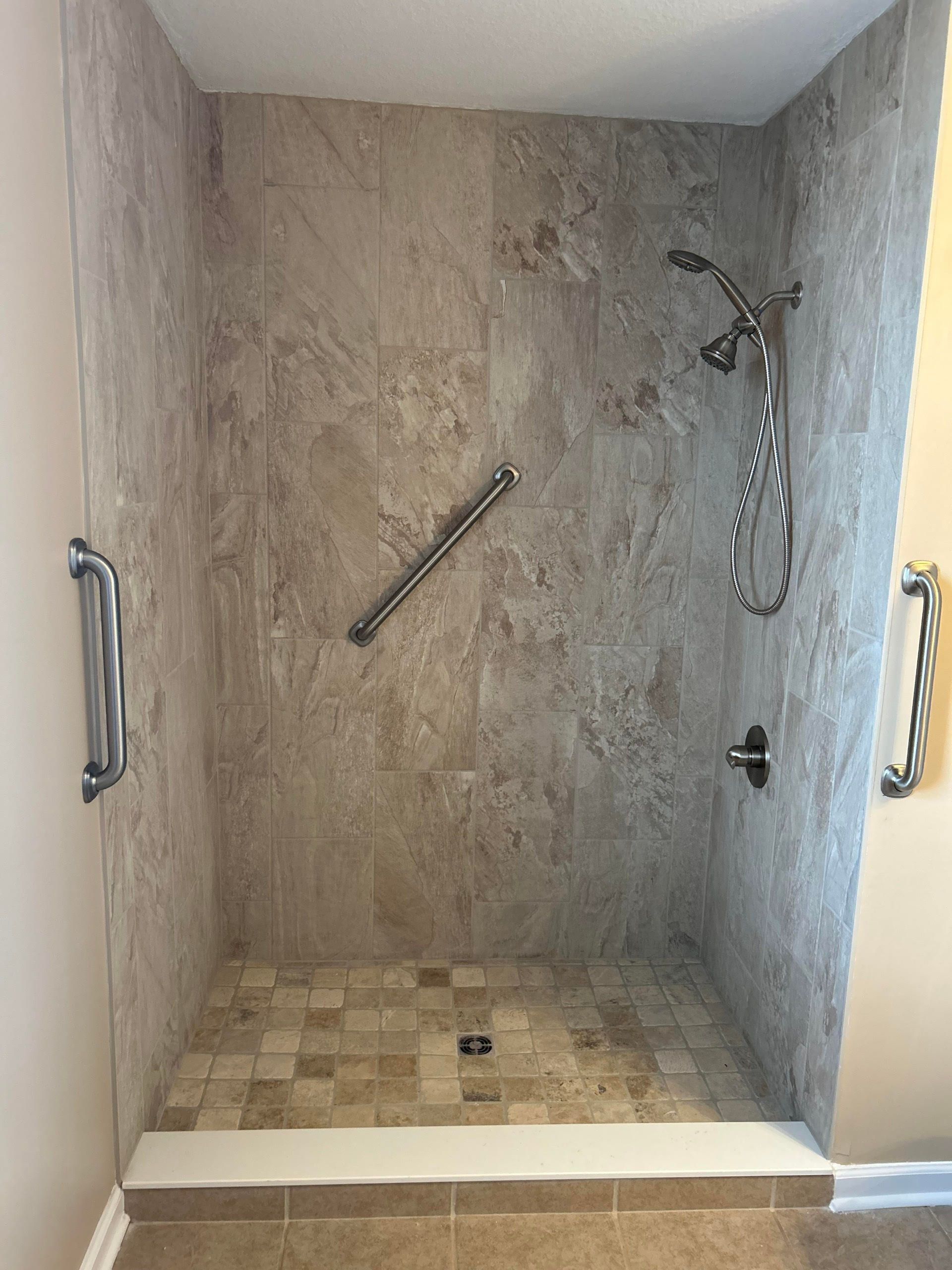 Empty walk-in shower with stone-look tile, bench ledge, and grab bars.