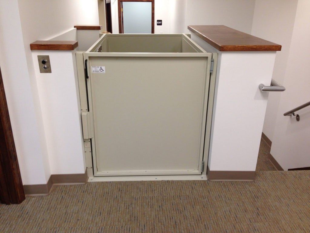Accessible platform lift with closed gate between stair railings in a hallway