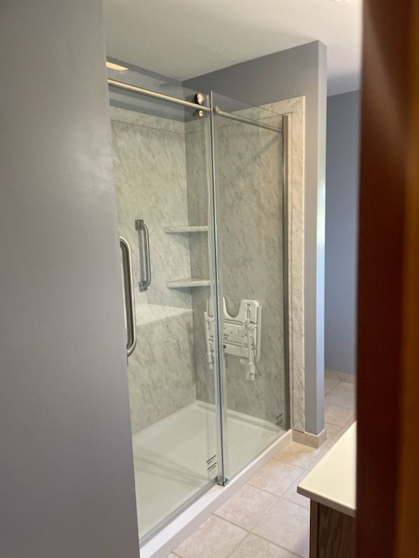 Glass-enclosed shower with marble-look tile, white tub, and chrome fixtures in a modern bathroom