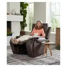 Person relaxing in a brown recliner with feet up in a bright living room, holding a cup.