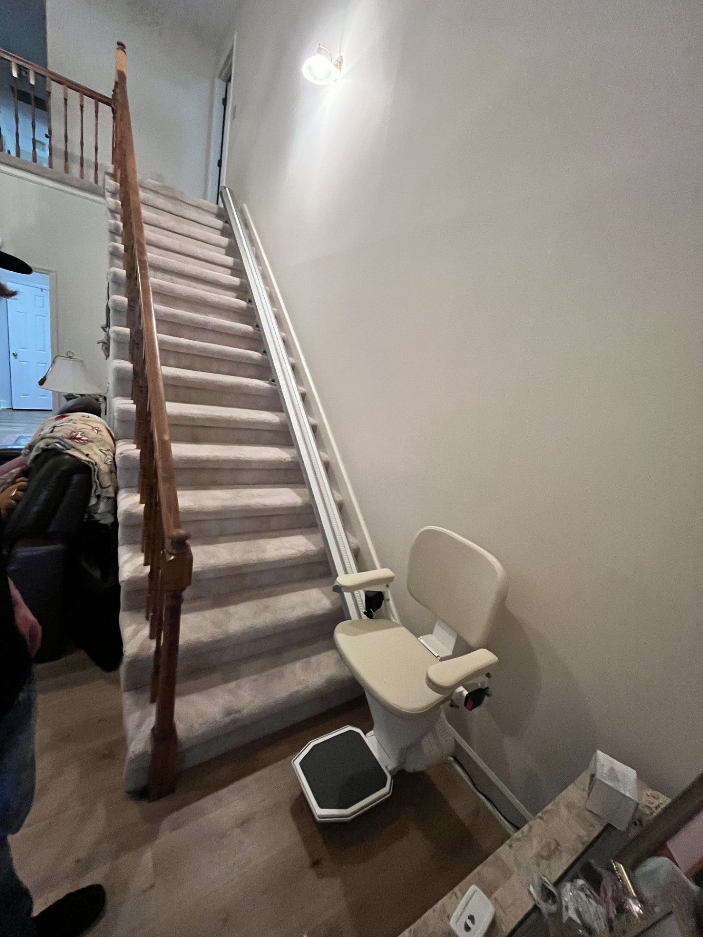 Narrow carpeted staircase beside a wall, with a stair lift chair and trash bin in a hallway.