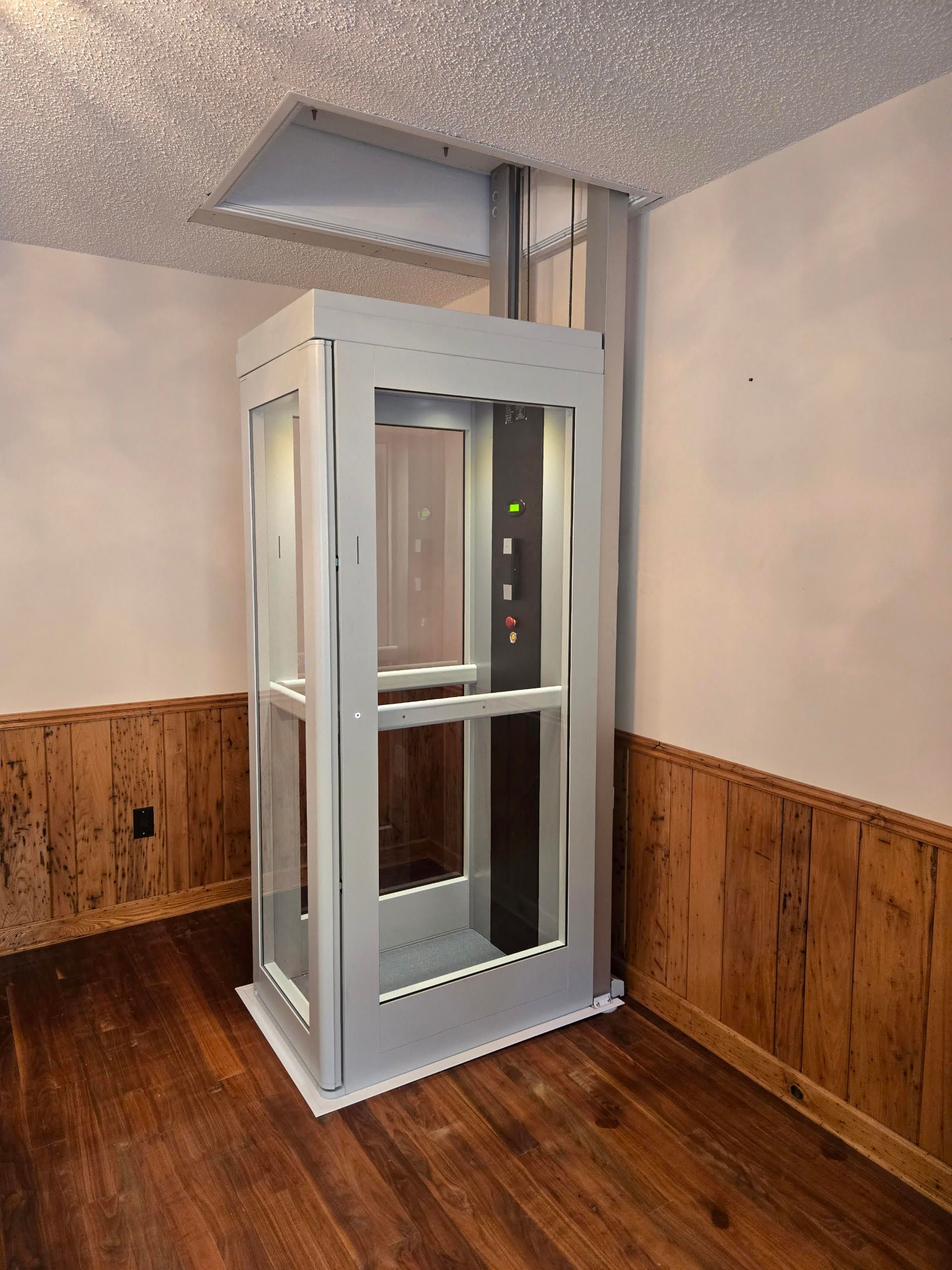 Residential elevator with glass doors in a room with wood wainscoting and hardwood floor
