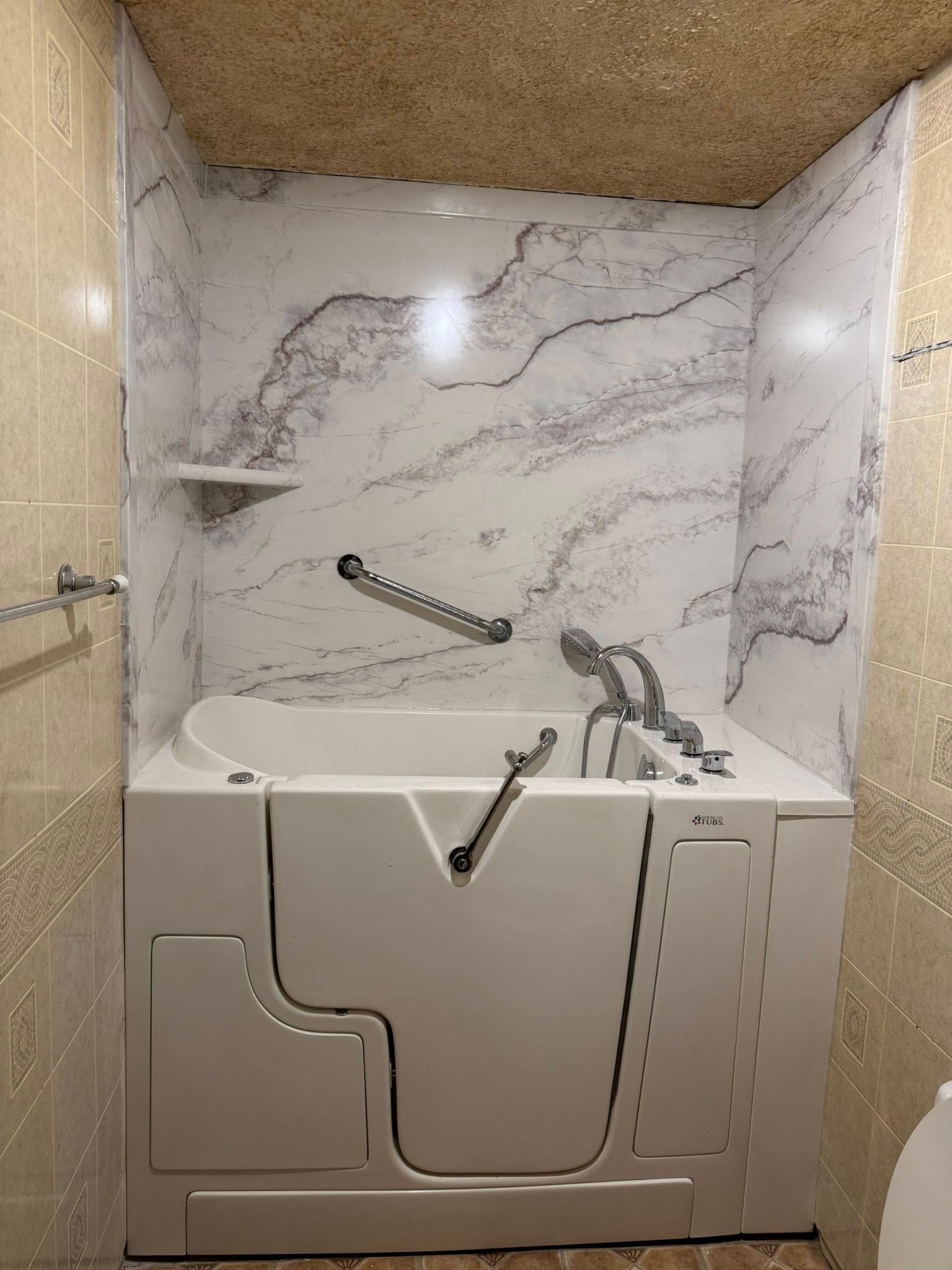 Accessible shower with grab bars, built-in seat, handheld showerhead, and marble-look walls.