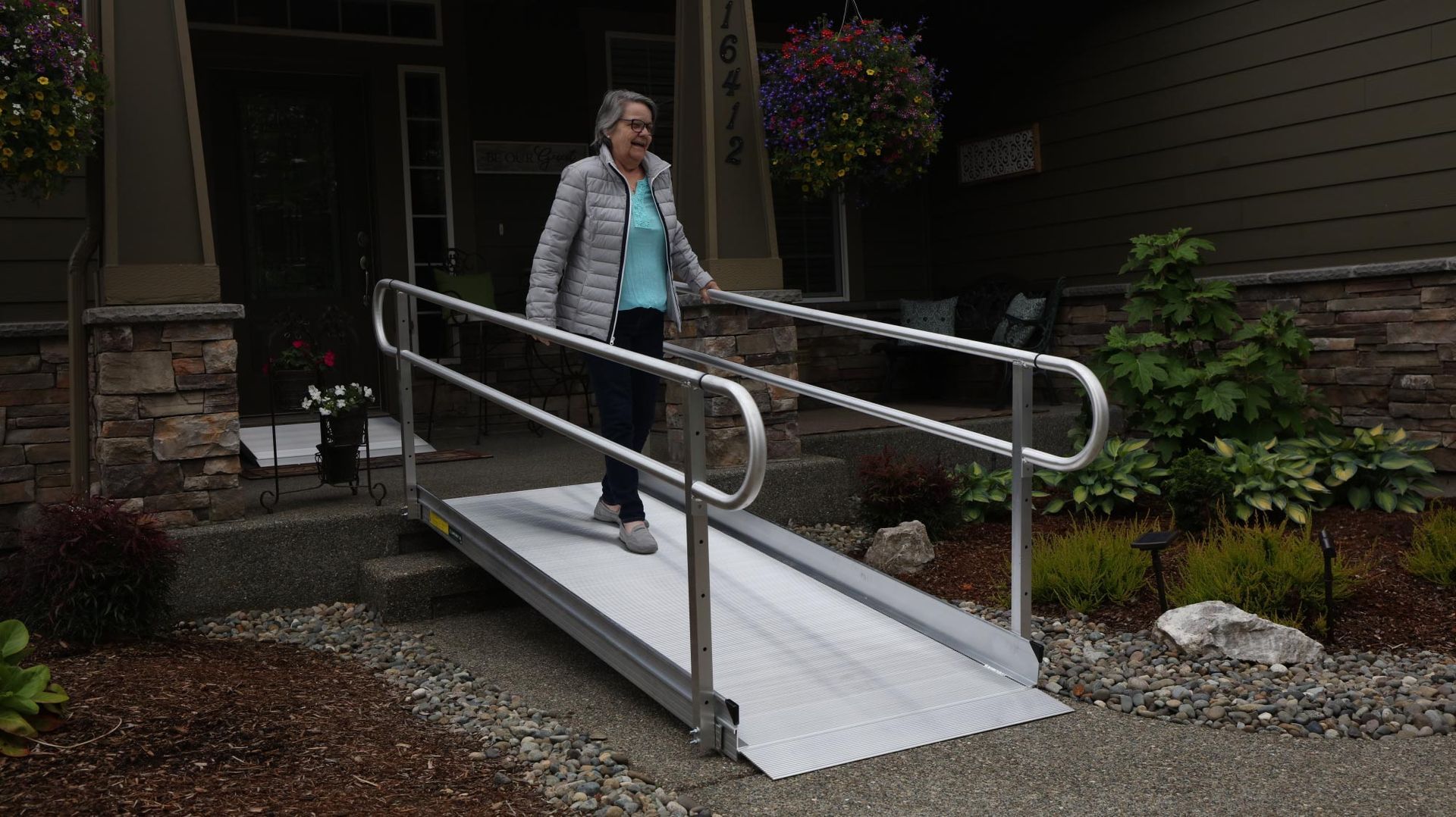 Person walking up an outdoor wheelchair ramp beside a house, with metal rails and white ramp surface