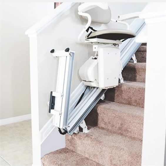 Motorized stair lift mounted on a carpeted staircase with a white railing and wall.