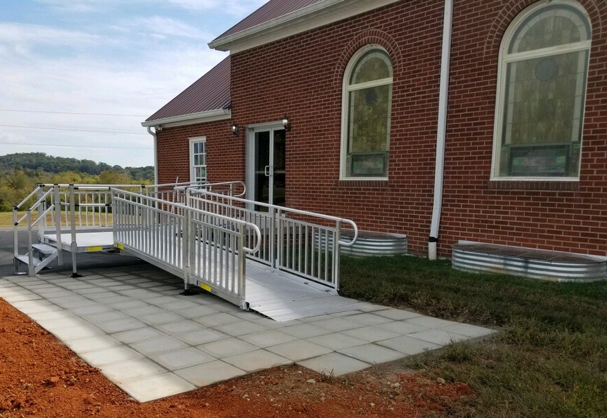 Brick house entrance with a wheelchair ramp, railings, and paved access path outdoors
