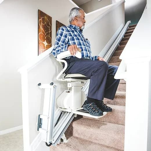Stairlift carrying a seated person up a carpeted staircase