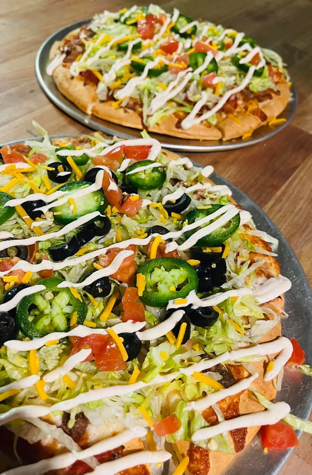 Two taco pizzas are sitting on a wooden table.
