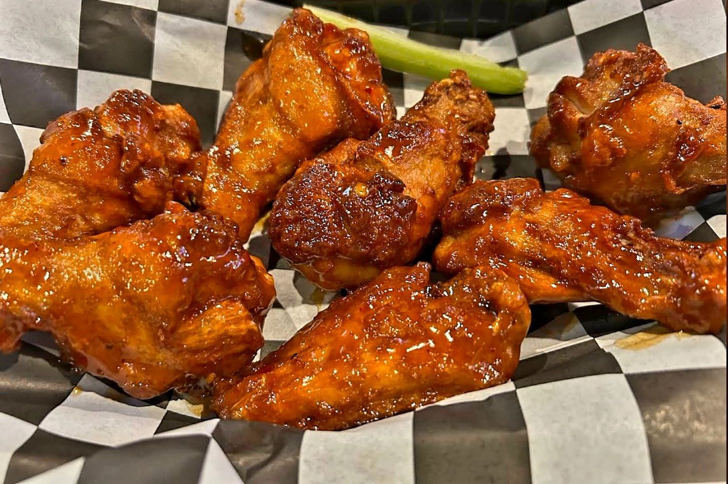 A basket of chicken wings with celery on a checkered paper.