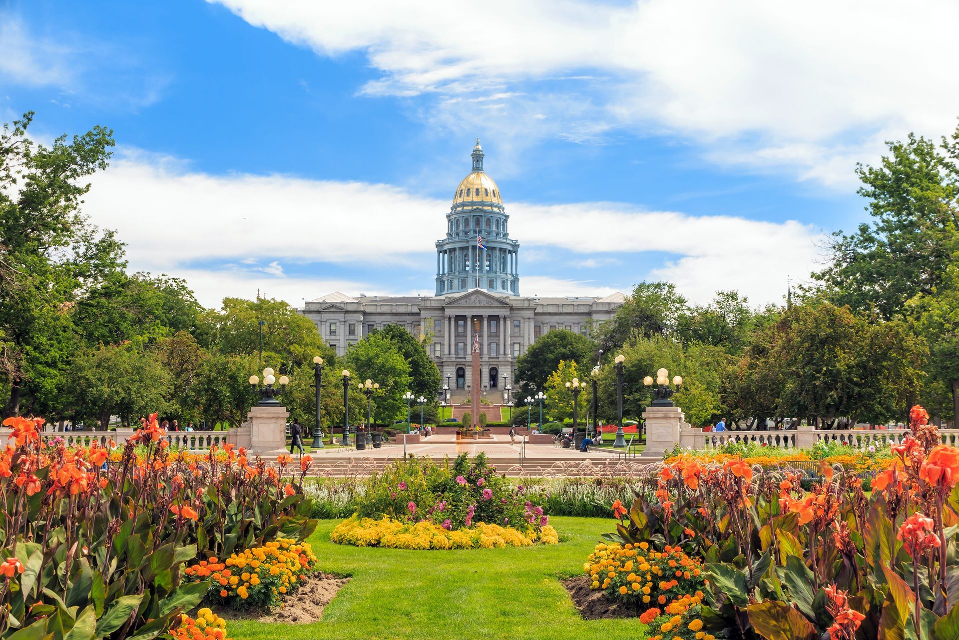 Colorado State Capitol building with golden dome, surrounded by colorful flowers and green lawn under a blue sky.
