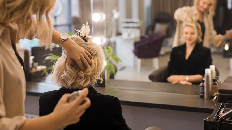 Hairdresser Styling a Client’s Blonde Hair in a Salon Mirror — Hair Truss & Co In Wallsend, NSW