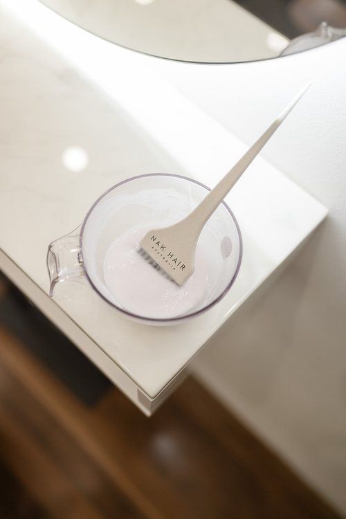 Wooden Cosmetic Spatula on a Clear Dish Atop a White Counter Beside a Sink — Hair Truss & Co In Wallsend, NSW