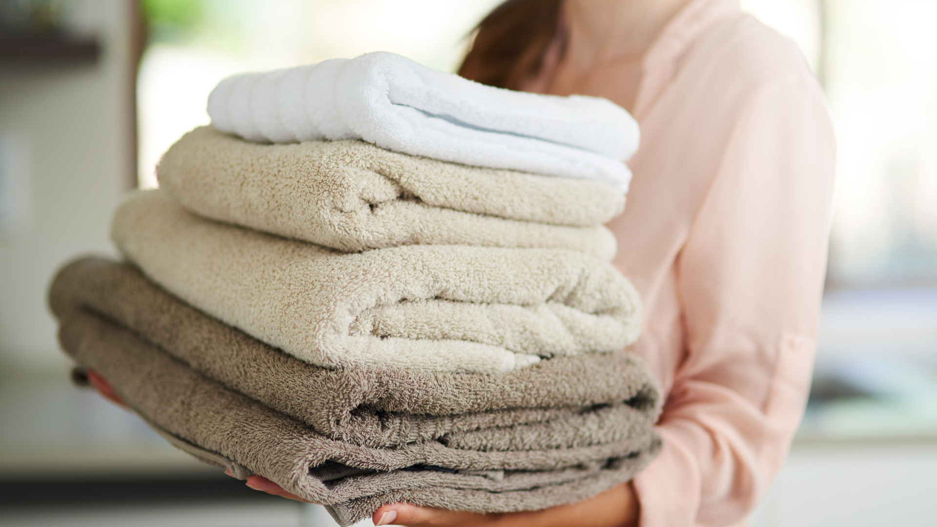 Person holding a stack of folded towels in varying shades of beige and white.