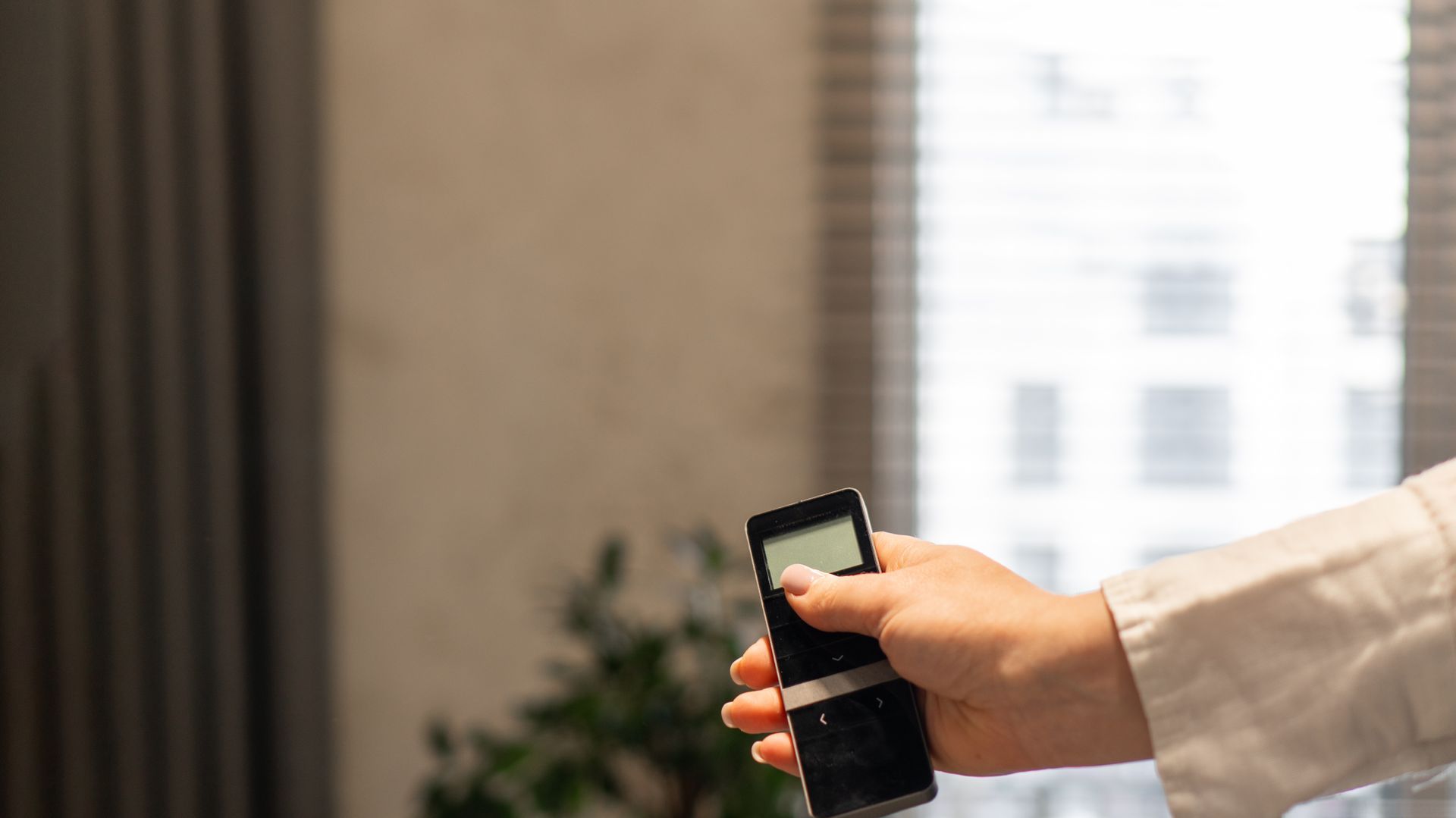 Hand holding a smartphone near a window in a bright office room