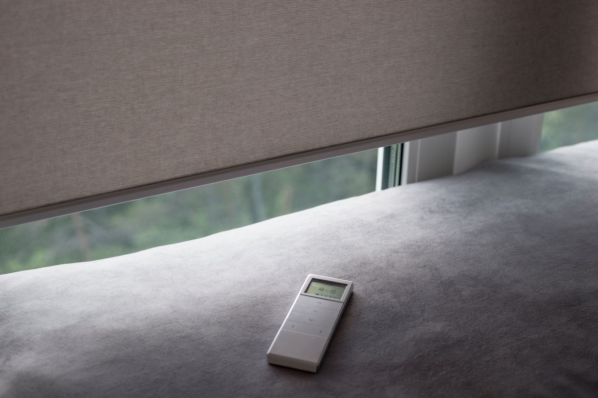 Custom motorized blinds partially lowered with remote control on modern windowsill.