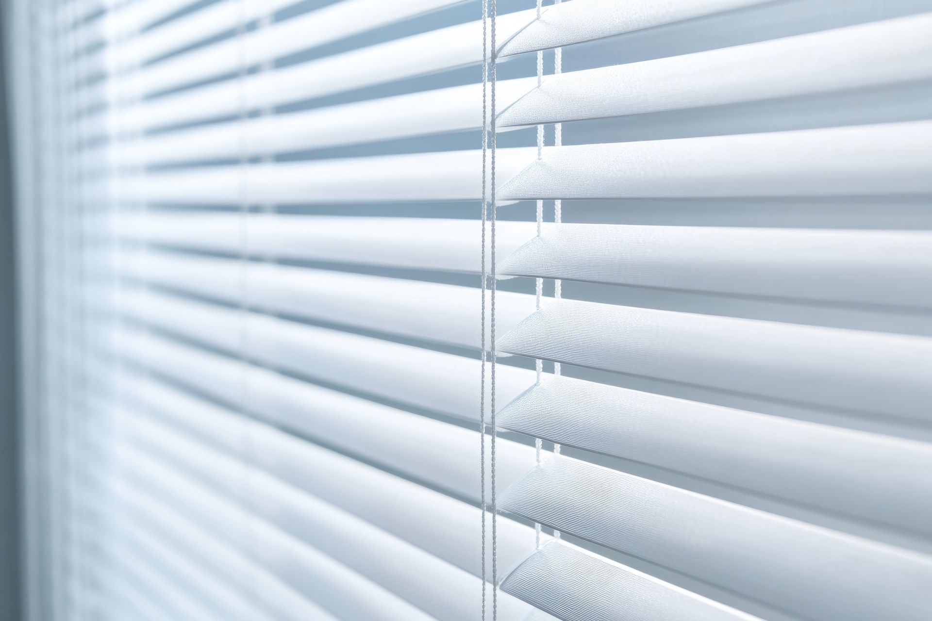 Close-up of white horizontal window blinds with soft light filtering through. Close-up of white horizontal window blinds with soft light filtering through.